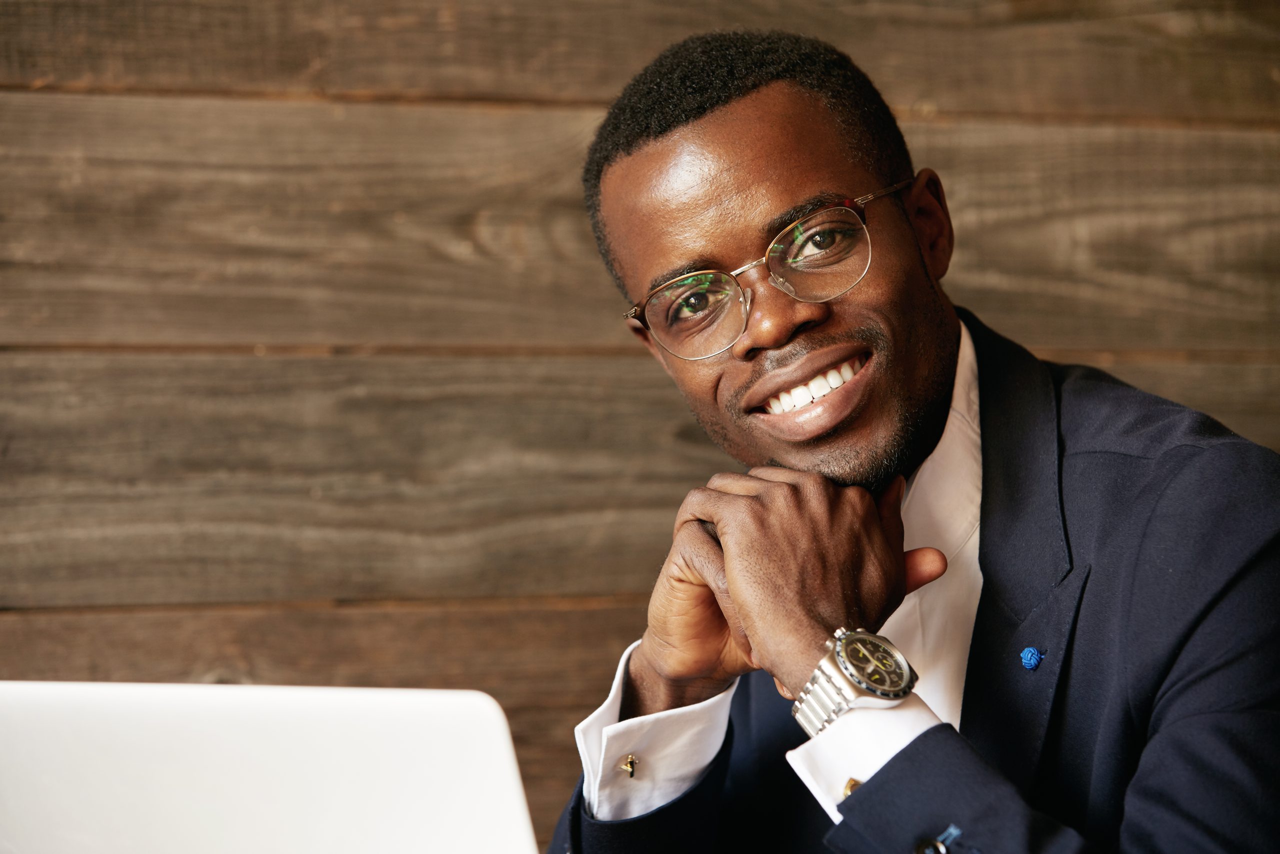 Portrait of handsome successful dark-skinned CEO in elegant suit and glasses, looking and smiling at the camera with happy confident expression, hands crossed. Career and achievement concept